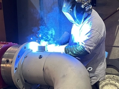 A large pipe flange being welded to a section of elbow pipe.